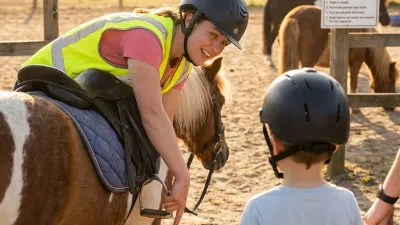 Ein Kind hält am Stall ein Schild „Bitte nicht füttern".
